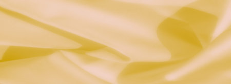 Blurred yellow fabric showcases smooth folds and gentle highlights, offering a warm and sophisticated texture for design and decorative uses.の写真素材