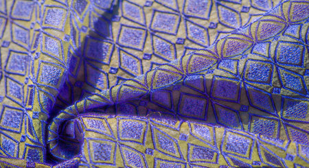 Blurred intricate geometric embroidery in blue and gold hues. The fabric's shimmering texture adds a...