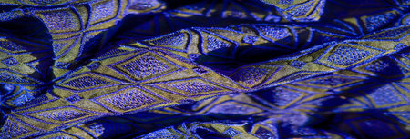 Blur of vibrant blue and gold fabric with geometric diamond patterns and shimmering texture,...