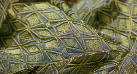 Blur close-up of a green and blue fabric featuring a textured diamond pattern with metallic...