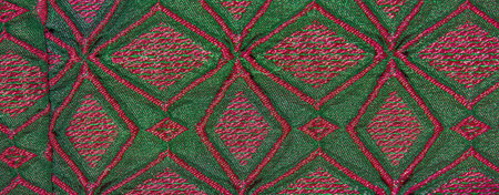 Blurred image of a colorful textured fabric featuring intricate pink and green geometric patterns....