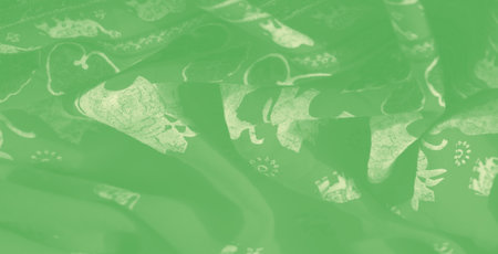 Blurred fabric with a green background and intricate floral patterns, showing smooth folds and soft textures. The light filtering through highlights the delicate details of the design,の写真素材