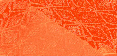 Blurred close-up shot of orange textured fabric with intricate geometric patterns and water...