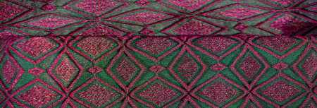 Blurred abstract fabric with intricate green and pink geometric patterns. The fabric features a...