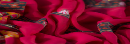 Blurred view of vibrant red fabric with intricate orange, white, and yellow floral patterns and glitter accents, showing a warm and colorful design aesthetic.の写真素材
