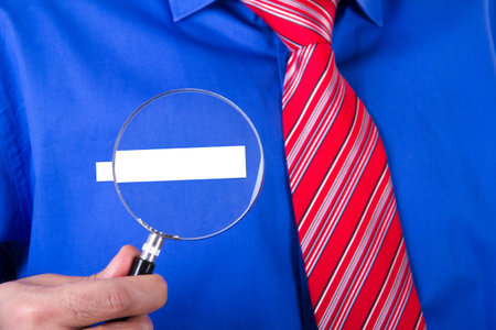 Businessman with red tie and blue shirt showing his blank label title with magnifying glass.の写真素材