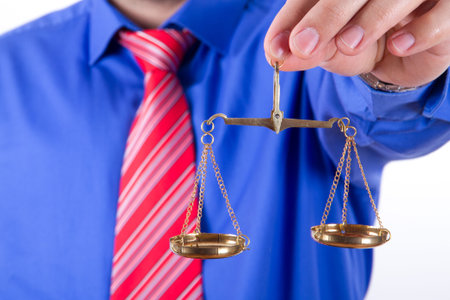 Businessman with red tie and blue shirt holding golden scales on balance, isolated on white...