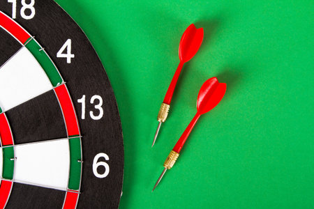 Dart board with black and white sections and red, plastic arrows on green background.