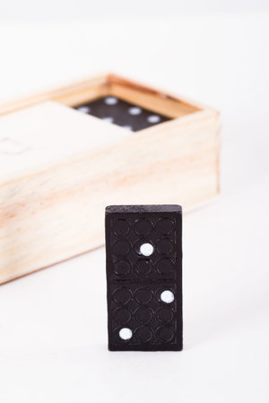 Black domino standing out from the dominoes in wooden box, isolated on white background.