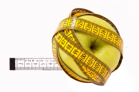 Green apples covered by yellow measure tape, isolated on white background.