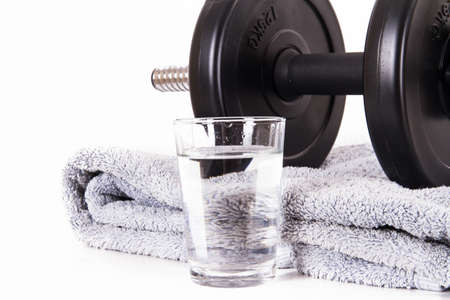 Black gym barbell, dumbbell with disks, blue towel and glass of water, isolated on white background.の写真素材