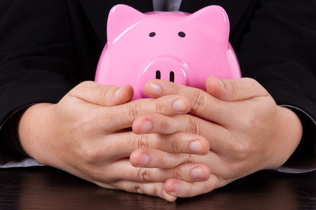 Business woman covering pink piggy bank.