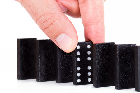 Hand holding black domino and building a line from dominoes, isolated on white background.