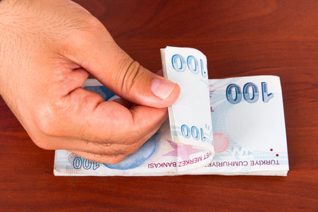 Hand countaing one hundred Turkish lira banknotes on wooden t able.