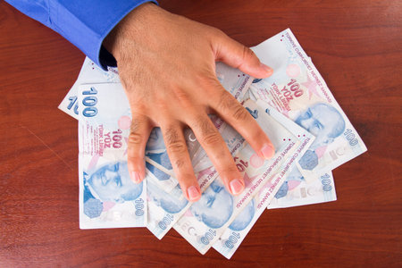 Hand on stack of one hundred Turkish lira banknotes on wooden table.の写真素材