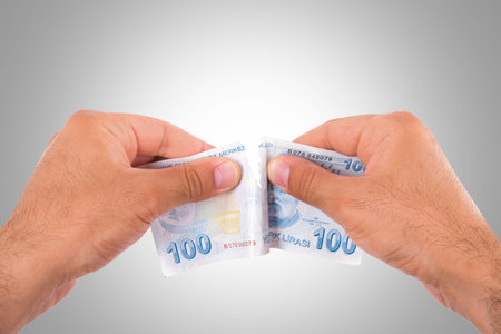 Hands tear one hundred Turkish lira banknote, isolated on white background.