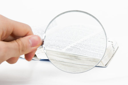 Classic style magnifying glass on open dictionary book, isolated on white background.