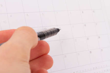 Desk or event calendar and hand holding pen which is pointing a day.
