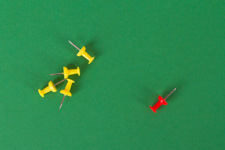 Red push pin standing out from yellows on green background.