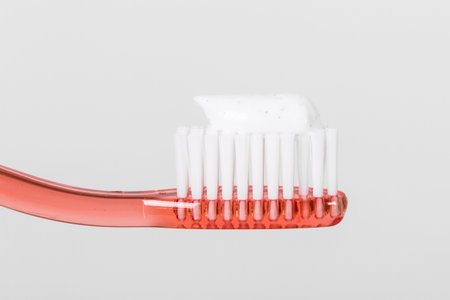 Side view of toothbrush with red plastic body, toothpaste on brushed, isolated on white background.