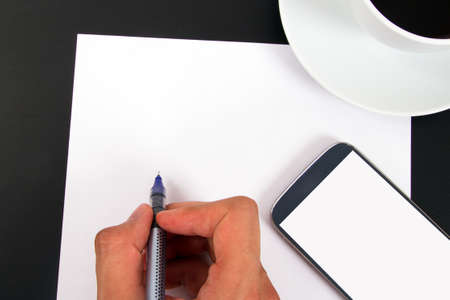Hand writing blank, white paper, smart phone with empty  screen, ceramic coffee cup top view on wooden table.の写真素材