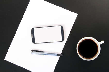 Smart phone with blank, white screen, ceramic coffee cup, pen and empty paper, top view on wooden table.の写真素材