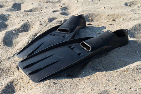 Black plastic flippers on sea sand.の写真素材