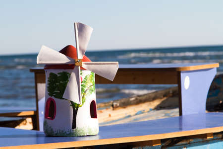 Toy wind mill on sailing boat at sea coast with clear, blue sky.の写真素材