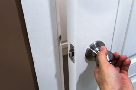 Hand holding door knob and opening white wooden door.