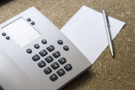 Telephone for customer service and blank white note paper with pen in hotel room.の写真素材
