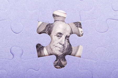 One  hundred dollar banknote between puzzle pieces.の写真素材