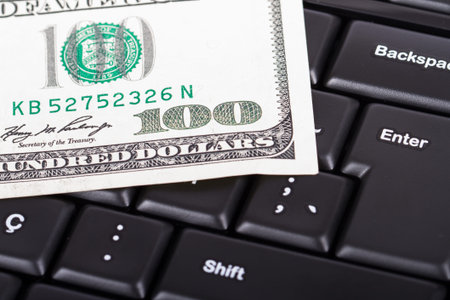 One hundred dollar bill on black computer keyboard.
