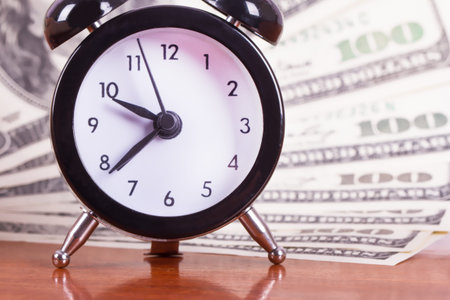 Finance concept, alarm clock and one hundred dollar banknotes on wooden table.
