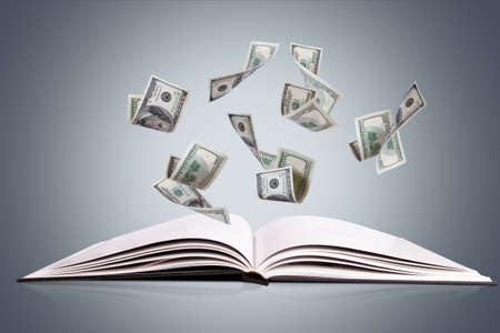 Open book or magazine with flying or falling one hundred dollar money banknotes on dark background.の写真素材
