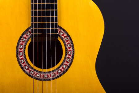 Front view of wooden classical acoustic guitar over black background.