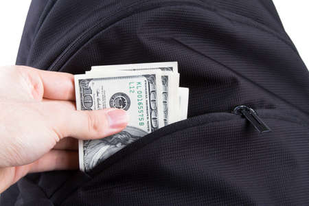 Hand putting dollar banknotes in back pack, isolated on white .の写真素材