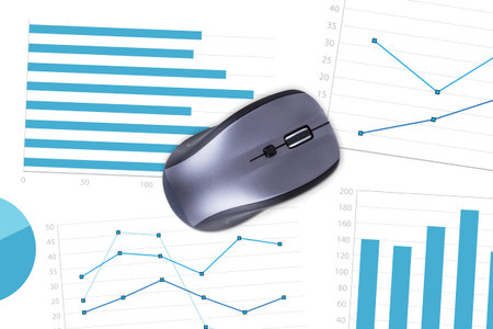 Top view of wireless computer mouse on paper sheet with financial statistic charts.