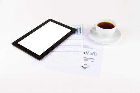 Black tablet with blank white screen and cup of tea on financial graph charts.の写真素材