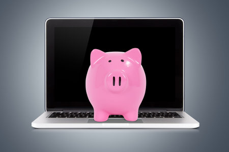 Laptop with blank screen and pink piggy bank for saving money on dark background.の写真素材