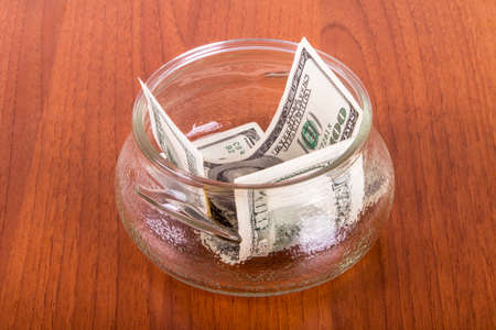 One hundred dollar banknotes in glass bowl on wooden table.の写真素材
