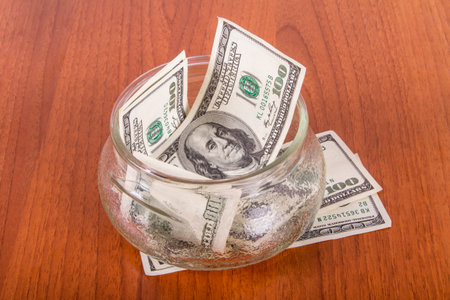One hundred dollar banknotes in glass bowl on wooden table.