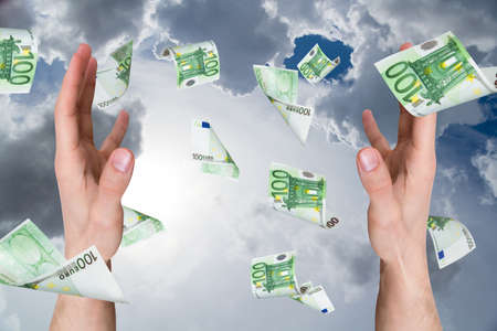 One hundred euro money banknotes flying and falling on young male hands on cloudy background.の写真素材