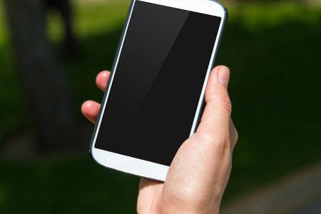 Close up view of smart phone with blank black screen on blurry natural background.