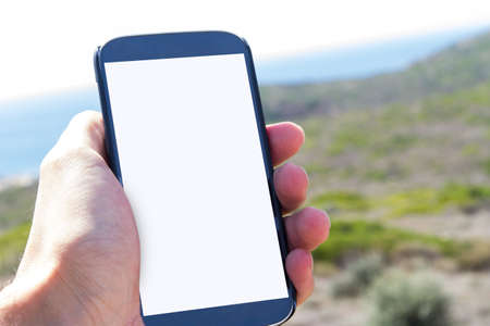 Male hand holding mobile phone with white blank screen mock up, copy space in nature.の写真素材