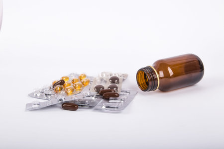 Close-up view of mix of pills and fallen brown glass medical bottle, isolated on white background.の写真素材