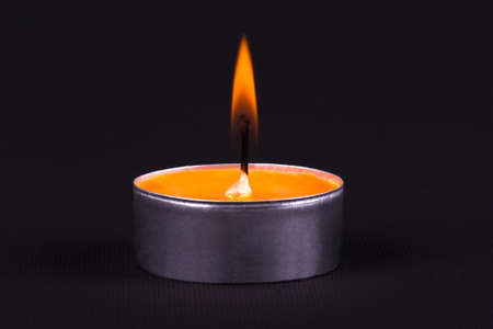 Close up detailed front view of burning orange candle, on black background.の写真素材