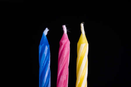 Close up front view of three multicolor birthday cake candles on black background.の写真素材