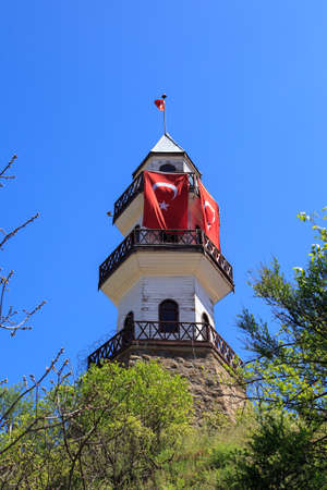 Buttom view of wooden tower building with Turkish flag waving, under blue sky.の写真素材