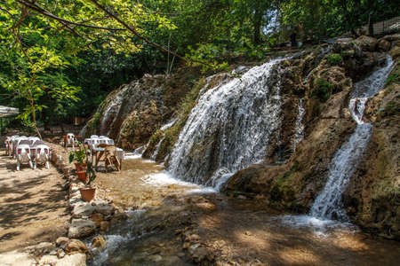 View of the tables and chairs near the flowing water of Harbiye Waterfall on natural rocks among trees.の写真素材