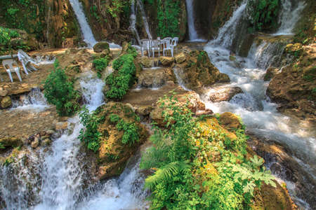 View of the tables and chairs near the flowing water of Harbiye Waterfall on natural rocks among trees.の写真素材